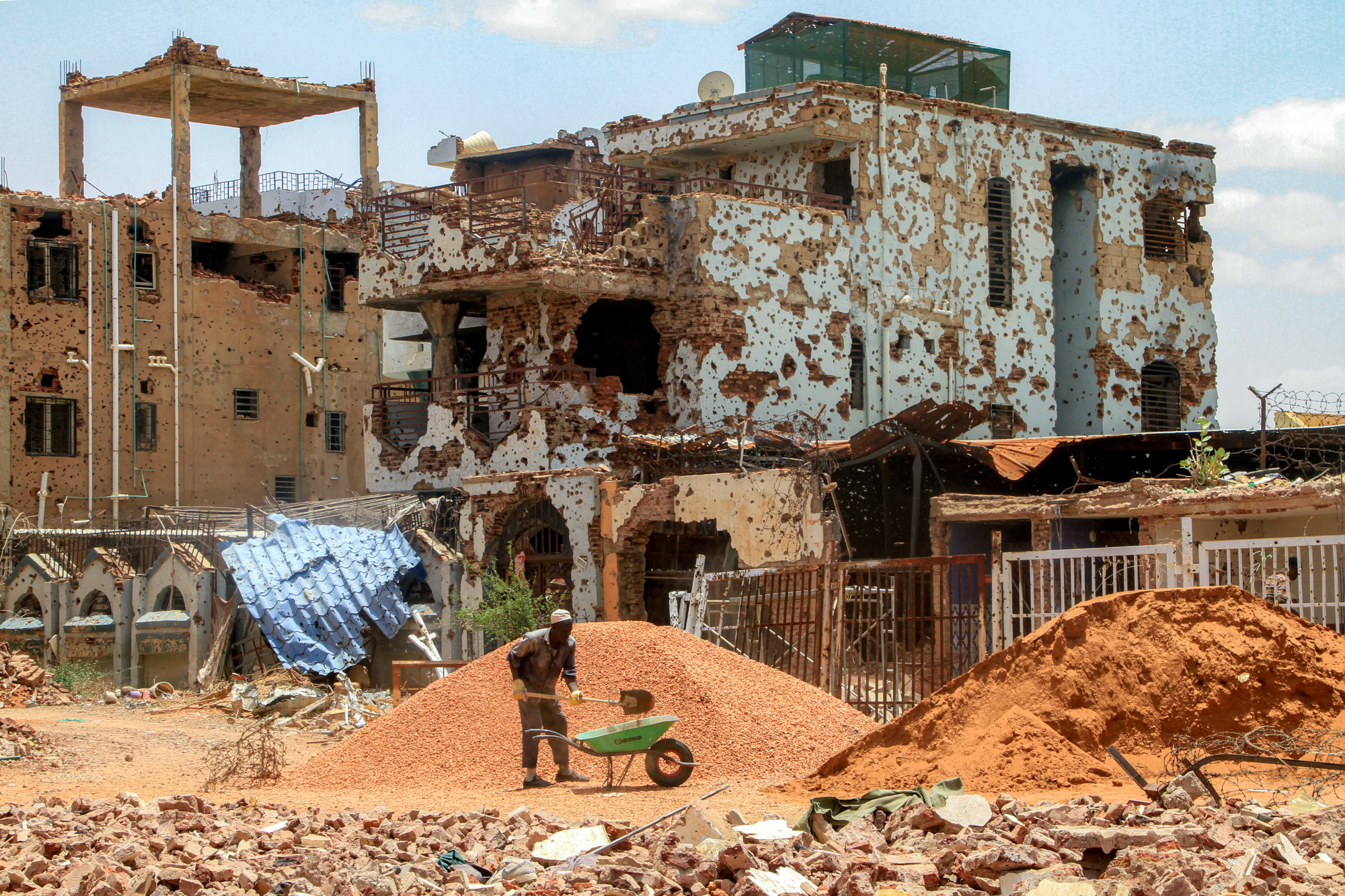 Una persona apalea tierra frente a un edificio bombardeado.