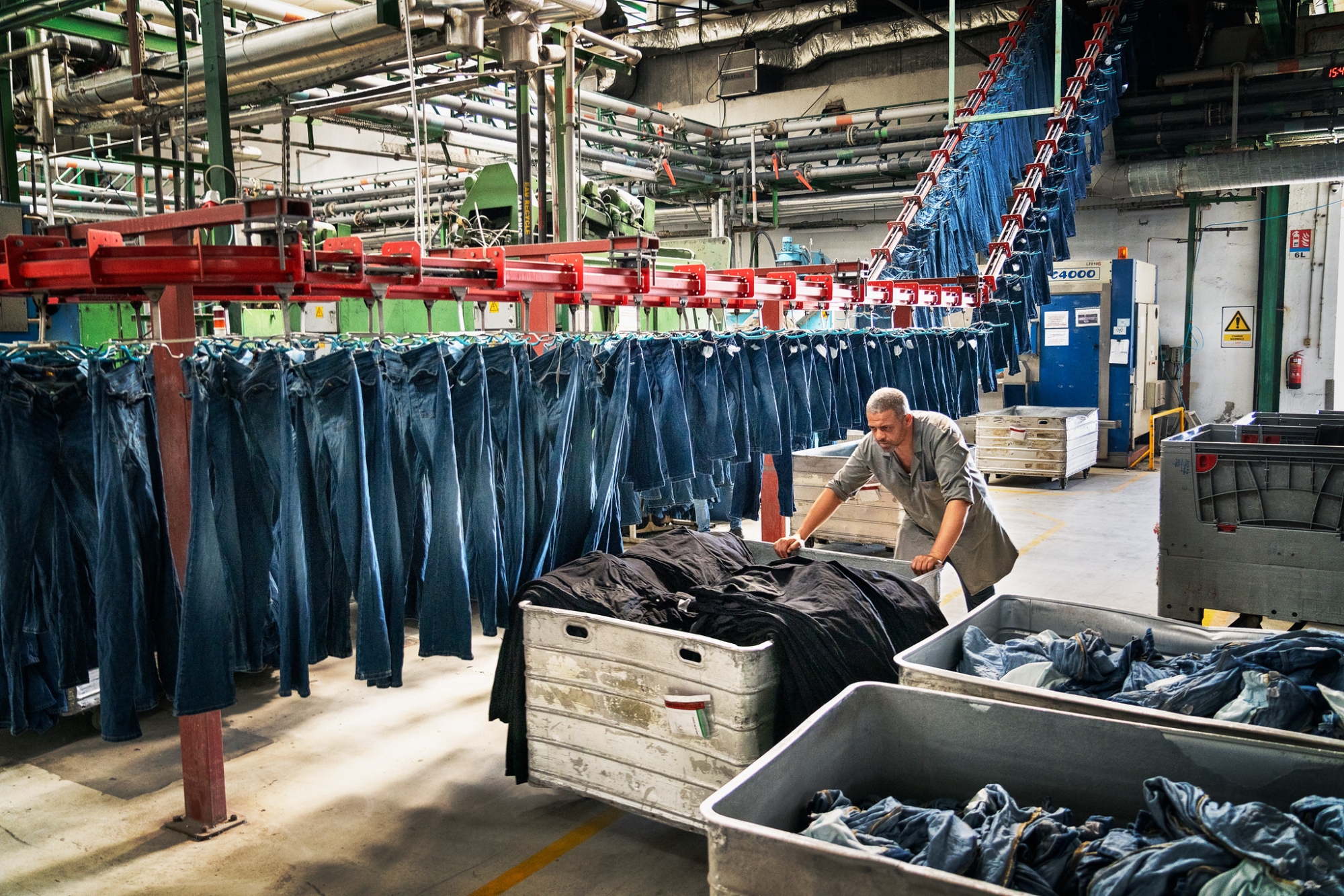 Un hombre empuja un carro lleno de jeans dentro de una fábrica.