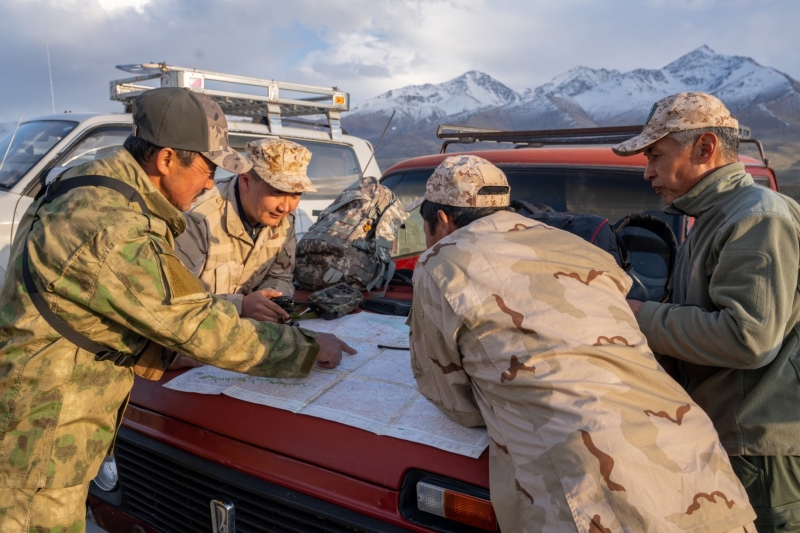 A group of men gather around a jeep.&nbsp;