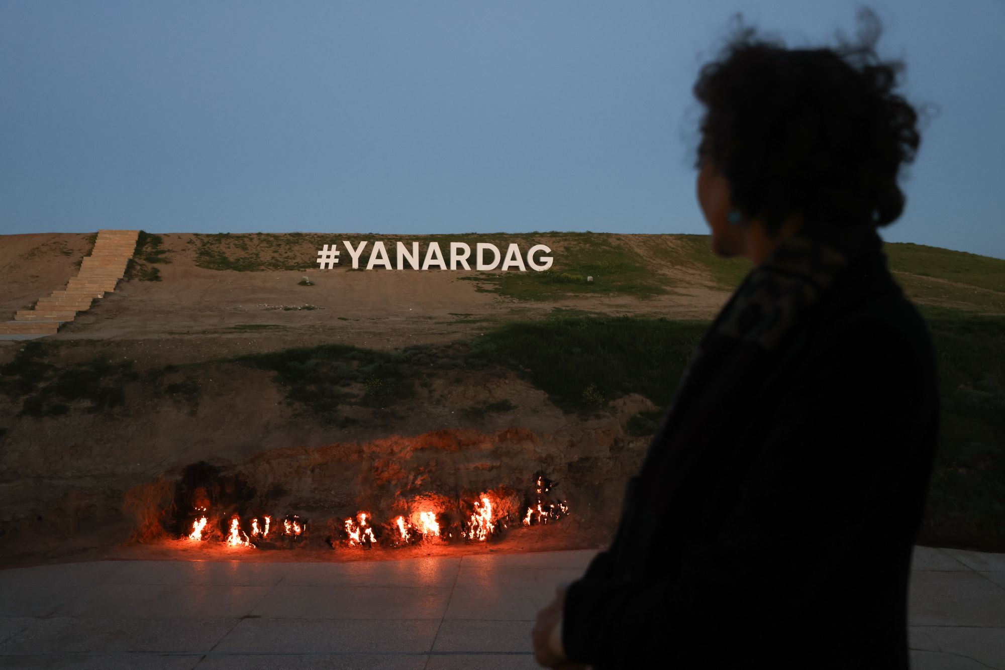 Flames burn in the distance as someone looks on