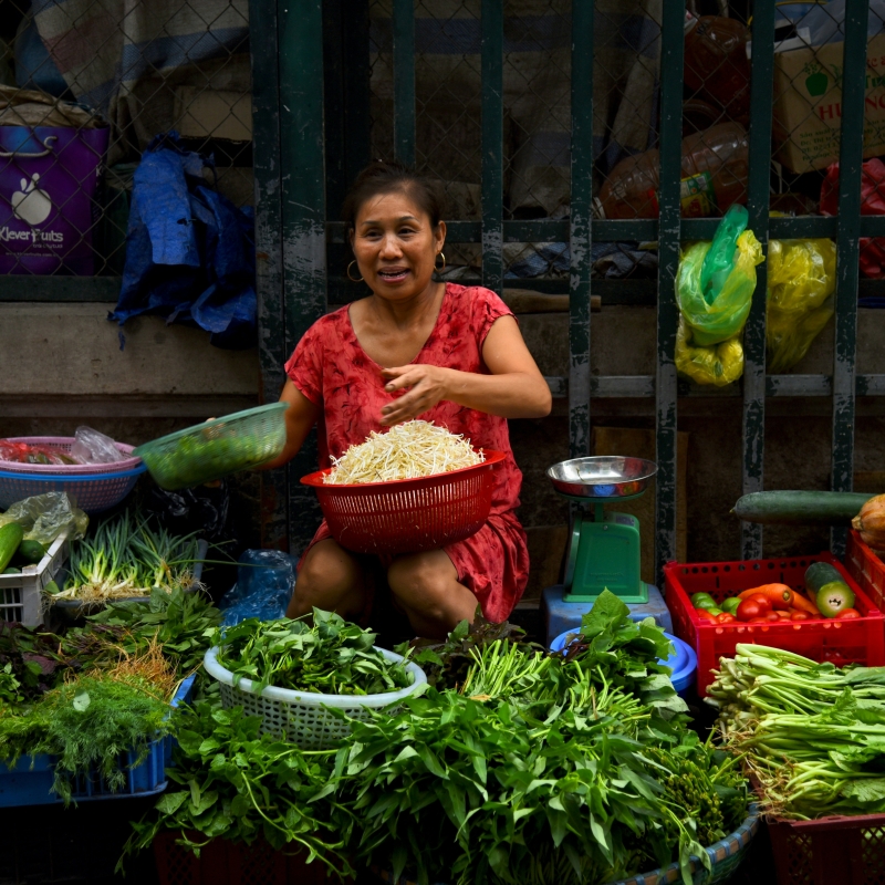 female vendor sits near weighing scale while selling vegetables