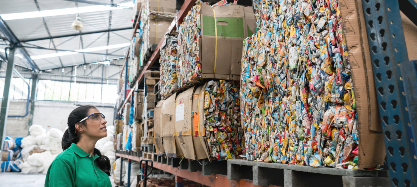 A woman working at a recycling plant reviews compressed recycled paper and plastic