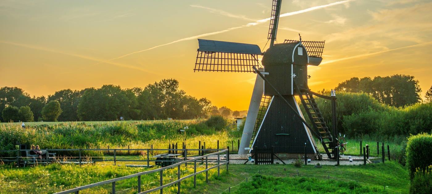 image of  black-and-white-wind-mill-in-green-field-under-yellow-skies-