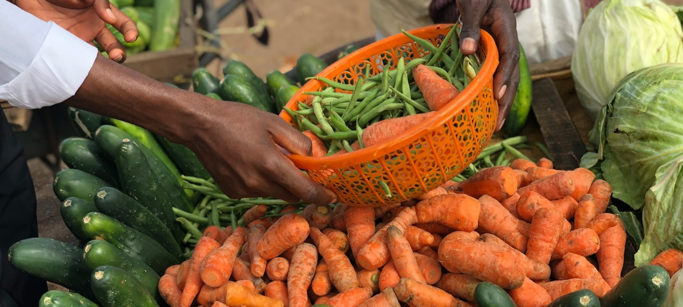 People passing each other produce at a market