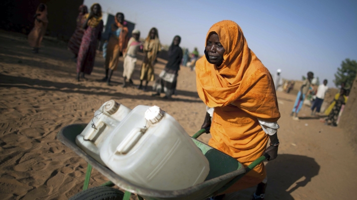 A woman pushes containers of water in a wheelbarrow 
