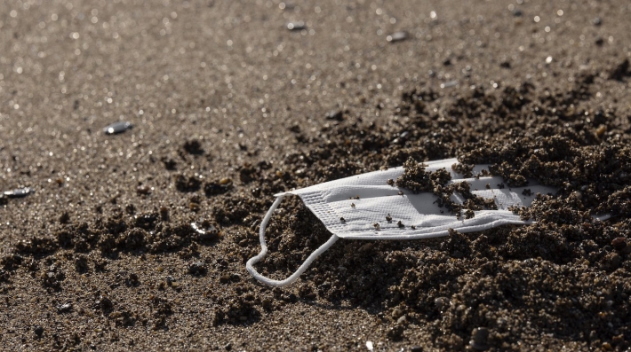 A face mask partially buried in sand.