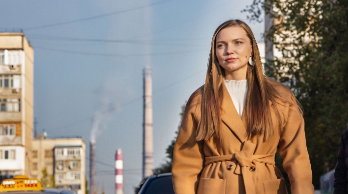 Женщина на улице с дымящей трубой за спиной.