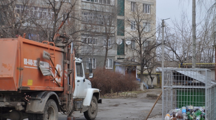 Garbage collection truck parked next to steel cage containing plastic and glass bottles
