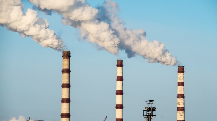 Three industrial smokestacks emitting white plumes of smoke