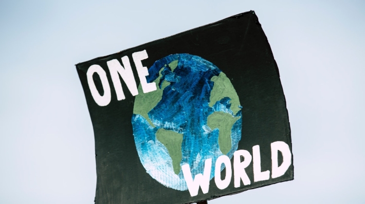 A sign with the text “ONE WORLD” printed over a painting of Earth