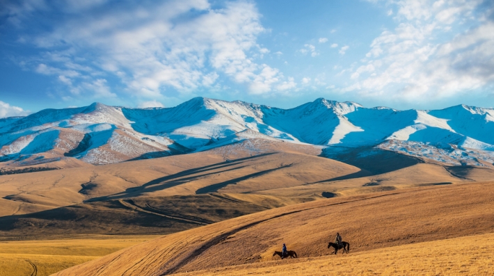 Two men on horseback riding across grasslands