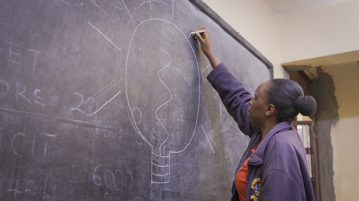 Teacher writing on a well-lit blackboard