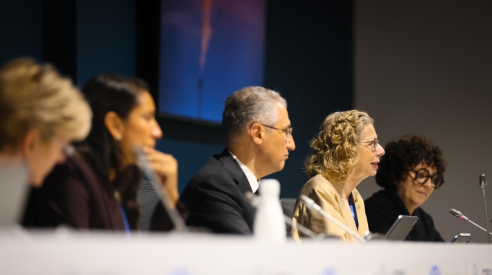 A group of people seated at a table on a stage, engaged in a discussion.