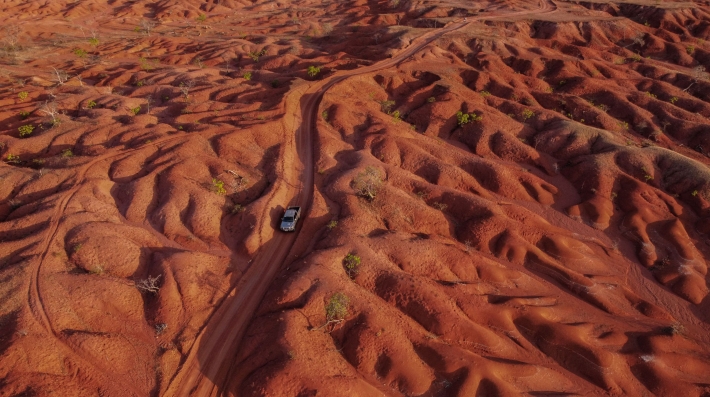 An aerial view of a pickup truck driving through a red sand desert. 