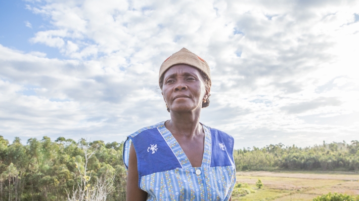 Una mujer de Madagascar mira a la distancia, bajo las nubes y frente a llanuras y bosques.