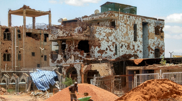 Una persona apalea tierra frente a un edificio bombardeado.