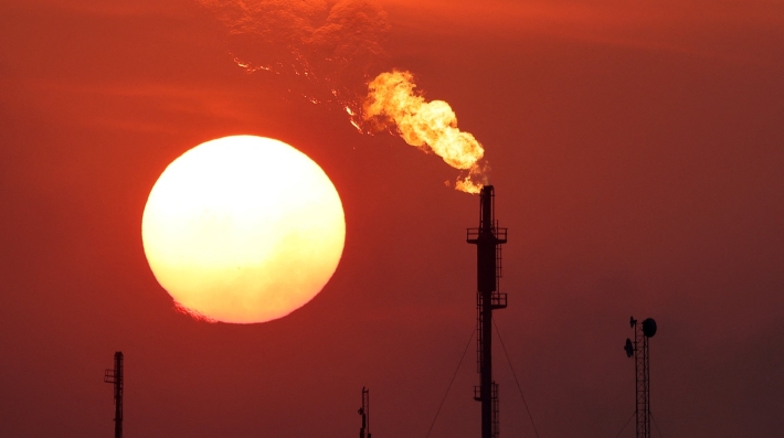 Una instalación petrolera emite una pluma de fuego con el sol poniente al fondo.